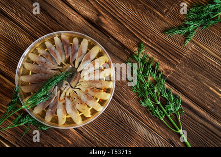 Fette di aringa scandinavo di filetto con spezie e aneto in un vasetto trasparente. Impostazione tabella su un rustico in legno tavolo fatto di tavole di pino Foto Stock