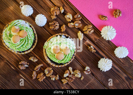 Torta, realizzato nella forma di un cestino con funghi, noci e meringa sono sul tavolo di tavole di pino. Marrone naturale e sfondo rosa. Diagonale. Foto Stock