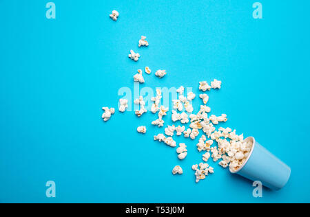 Salate fresche pop corn versato al di fuori di un contenitore in cartone, blu colore di sfondo, spazio copia Foto Stock
