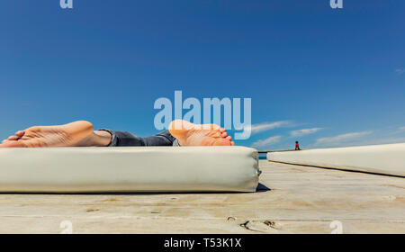 Le suole del giovane uomo con i piedi sul materasso bianco con cielo blu in background Foto Stock