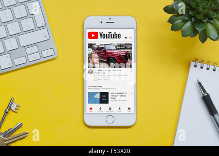Un iPhone che mostra il sito web YouTube poggia su uno sfondo giallo tabella con una tastiera, tasti, blocco note e di impianto (solo uso editoriale). Foto Stock