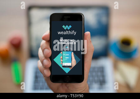 Un uomo guarda al suo iPhone che visualizza il logo Wealthify (solo uso editoriale). Foto Stock