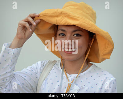 Giovane donna tailandese con begli occhi indossa un moderno floppy hat e sorrisi per la fotocamera. Foto Stock