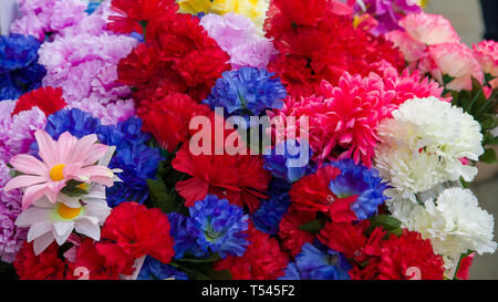 Una colorata serie di di fiori di plastica sul display al di fuori di un negozio locale. Foto Stock