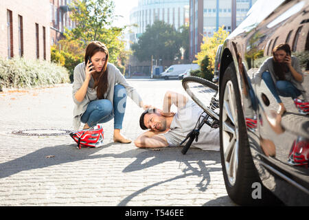 Giovane donna chiamando ambulanza dopo colpire ciclista maschio accidentalmente con la sua automobile Foto Stock