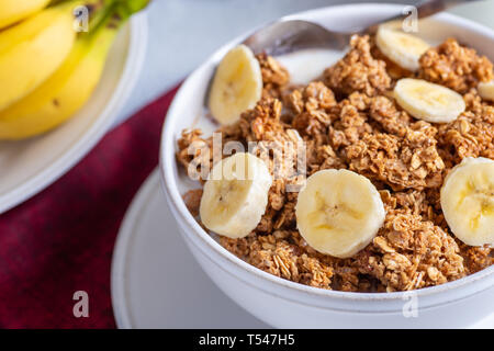 Primo piano di una ciotola di granola witk fette di banana e latte con le banane in background Foto Stock