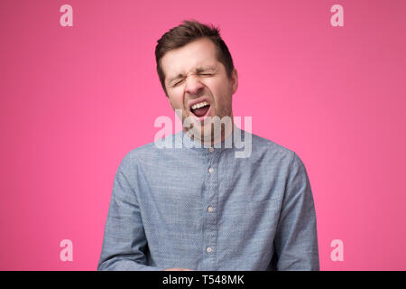Stanco uomo sente assonnato, sbadigli come si sente stanco, apre la bocca ampiamente, pone su sfondo rosa. Foto Stock