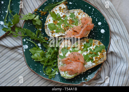 Panini con pesce rosso, la crema di formaggio, rucola, la senape, le spezie verde sulla piastra in ceramica con puntini bianchi. Una sana colazione con salmone. Alla moda di foo Foto Stock