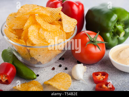 Ciotola di vetro piatto con patatine chips con paprica e peperoncino su sfondo chiaro. Il rosso e il verde la paprica pepe con patate e piccante Foto Stock