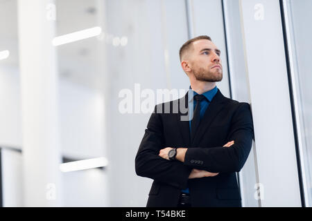Ritratto di giovane fiducioso elegante uomo d affari con due mani incrociate vicino alla finestra. Foto Stock