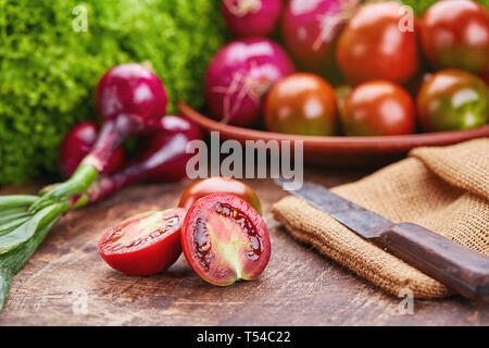 Su un tavolo di legno cipolla, pomodori verdi e i coltelli. Foto Stock