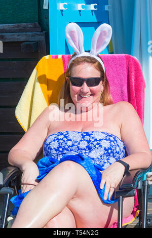 Bournemouth Dorset, Regno Unito. 21 apr 2019. Regno Unito: meteo canicola continua con caldo e soleggiato, come testa beachgoers al mare per godere del calore e del sole a Bournemouth spiagge per le vacanze di Pasqua - metà mattina e già le spiagge sono sempre imballati, come sunseekers arrivarci presto per ottenere il loro spazio. Vestito per l'occasione! Donna che indossa Easter Bunny orecchie rilassanti bagni di sole al beach hut. Credito: Carolyn Jenkins/Alamy Live News Foto Stock