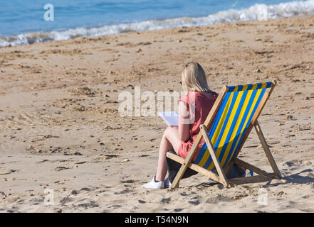 Bournemouth Dorset, Regno Unito. 21 apr 2019. Regno Unito: meteo canicola continua con caldo e soleggiato, come testa beachgoers al mare per godere del calore e del sole a Bournemouth spiagge per le vacanze di Pasqua - metà mattina e già le spiagge sono sempre imballati, come sunseekers arrivarci presto per ottenere il loro spazio. Donna seduta in sedia a sdraio la lettura del libro. Credito: Carolyn Jenkins/Alamy Live News Foto Stock