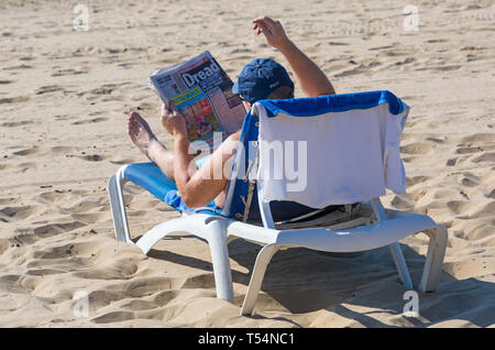 Bournemouth Dorset, Regno Unito. 21 apr 2019. Regno Unito: meteo canicola continua con caldo e soleggiato, come testa beachgoers al mare per godere del calore e del sole a Bournemouth spiagge per le vacanze di Pasqua - metà mattina e già le spiagge sono sempre imballati, come sunseekers arrivarci presto per ottenere il loro spazio. L uomo a prendere il sole sul lettino la lettura del quotidiano Sun. Credito: Carolyn Jenkins/Alamy Live News Foto Stock