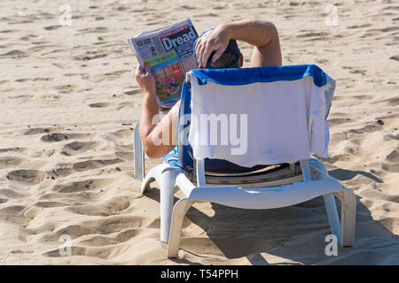 Bournemouth Dorset, Regno Unito. 21 apr 2019. Regno Unito: meteo canicola continua con caldo e soleggiato, come testa beachgoers al mare per godere del calore e del sole a Bournemouth spiagge per le vacanze di Pasqua - metà mattina e già le spiagge sono sempre imballati, come sunseekers arrivarci presto per ottenere il loro spazio. L uomo a prendere il sole sul lettino la lettura del quotidiano Sun. Credito: Carolyn Jenkins/Alamy Live News Foto Stock