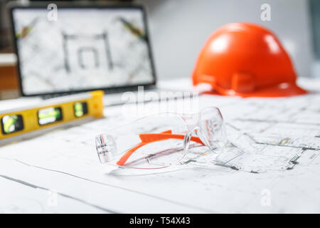 Costruzione degli occhiali di protezione,arancio elmetto, laptop con disegni, misuratore di livello giacente in un blueprint su un tavolo. Architettura e Costruzione Foto Stock