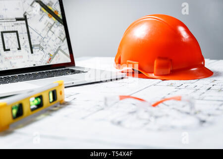 Orange elmetto, laptop con disegni, misuratore di livello e occhiali protettivi giacente in un blueprint su un tavolo. Architettura e costruzione concept Foto Stock