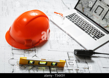 Orange elmetto, laptop con disegni, bicchieri e walkie-talkie con blueprint su un tavolo. Architettura e costruzione concept Foto Stock