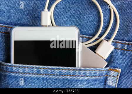 White smart phone con potere bancari nella tasca dei jeans. smart phone è in carica dalla banca di potenza Foto Stock