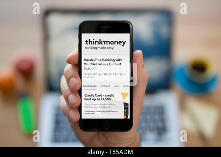 Un uomo guarda al suo iPhone che visualizza il logo Thinkmoney (solo uso editoriale). Foto Stock