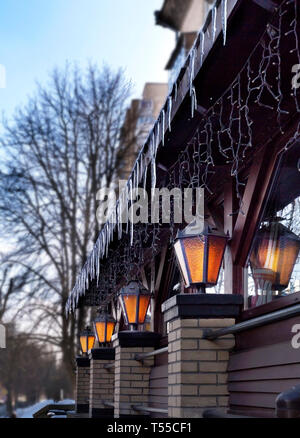 Quattro vecchi lampioni brillare vicino al ristorante windows all'aria aperta nei primi mattina di primavera. Icy ghiaccioli guardare in giù su di essi. Foto Stock