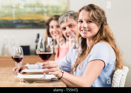 Donna che mantiene il vetro di vino seduti con la famiglia Foto Stock