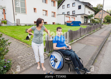 Madre e figlio disabile in attesa per il bus di scuola Foto Stock