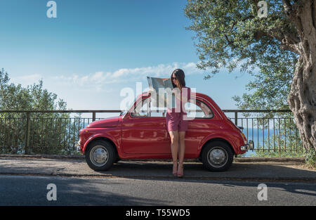 Donna che mantiene mappa poggiando su auto rosa Foto Stock