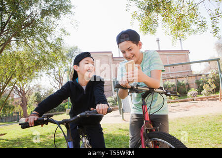 Ragazzi guardando smart phone sul loro biciclette Foto Stock