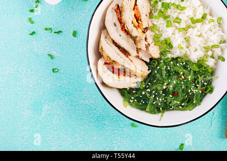 Una sana insalata in una ciotola bianco, bastoncini. Involtini di pollo, riso, chuka e cipolla verde. Sfondo blu. Cucina asiatica. Vista superiore Foto Stock