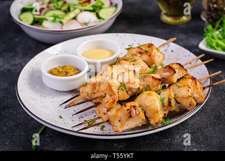 Grigliata di spiedini di pollo e con insalata di cetrioli, Rafano, cipolla su uno sfondo scuro. Foto Stock