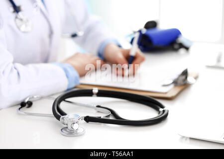 Primo piano dello stetoscopio. Medico donna riempie la forma medica mentre seduto alla scrivania in ospedale. Sanità, Workplace e cardiologia in medicina Foto Stock