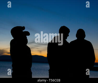 Silhouette di tre fratelli a bere birra e guardare il tramonto sulla spiaggia Foto Stock