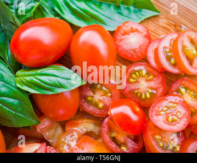 Tritate i pomodori ciliegini e basilico su un tagliere Foto Stock