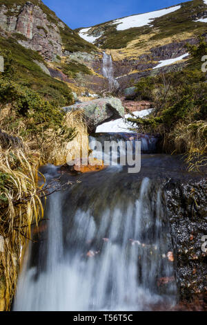Basso in prospettiva di grandi, Scenic, bella cascata acqua che cade dal rosso scogliera rocciosa sotto la neve Foto Stock
