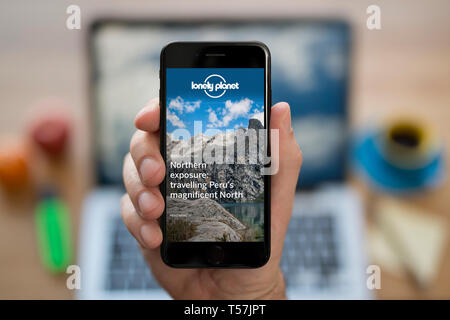 Un uomo guarda al suo iPhone che consente di visualizzare la guida della Lonely Planet logo (solo uso editoriale). Foto Stock