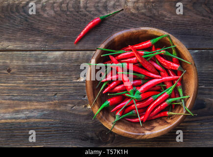 Piccole organiche peperoncino rosso in ciotola di legno rustico sfondo. Vista dall'alto. Foto Stock