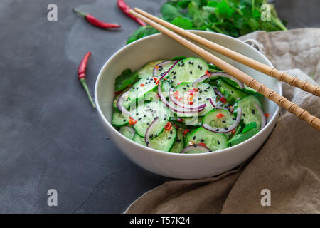 Asian insalata di cetrioli con cipolla rossa, peperoncino e sesamo nero in bianco ciotola sul cemento grigio Sfondo. Foto Stock