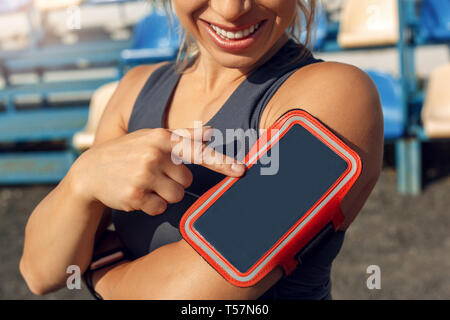 Donna giovane atleta che indossa fascia permanente sulla stadium stile di vita sportiva toccando lo schermo dello smartphone protector sorridendo felice close-up Foto Stock