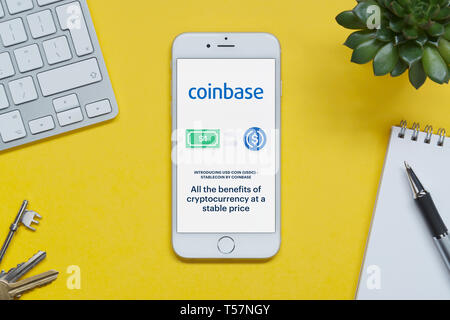 Un iPhone che mostra il sito web Coinbase poggia su uno sfondo giallo tabella con una tastiera, tasti, blocco note e di impianto (solo uso editoriale). Foto Stock