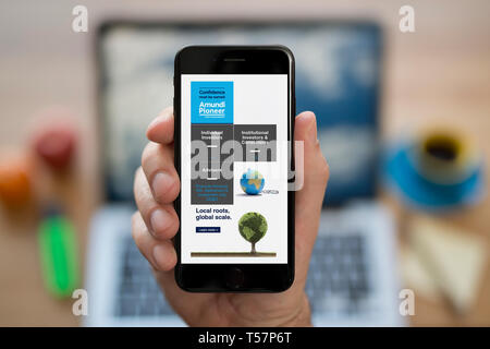 Un uomo guarda al suo iPhone che visualizza il Amundi Asset Management logo (solo uso editoriale). Foto Stock