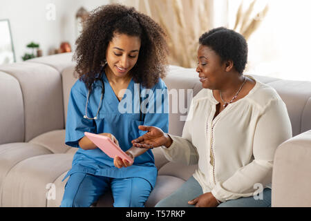 Anziani di carnagione scura lady sensazione gioiosa mentre parla a un infermiere Foto Stock