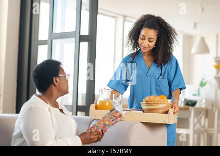 Giovane assistente medico portando un po' di cibo per signora anziana Foto Stock