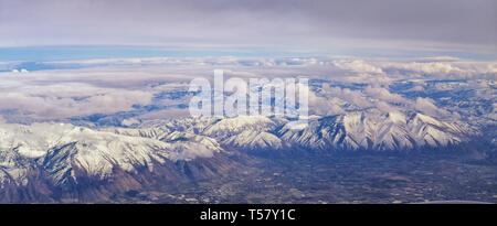Vista aerea da aereo di Wasatch Rocky Mountain Range con cime innevate in inverno comprese città urbane di Provo, Farmington Bount Foto Stock
