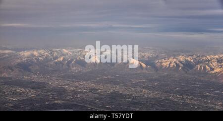 Vista aerea da aereo di Wasatch Rocky Mountain Range con cime innevate in inverno comprese città urbane di Provo, Farmington Bount Foto Stock