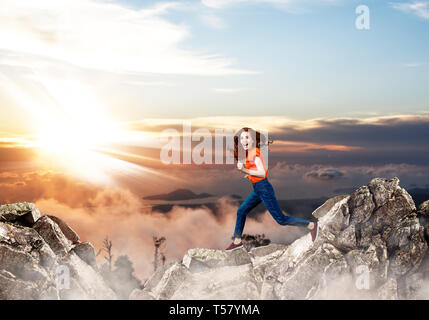 Redhead donna passa attraverso lo spazio tra le colline sulla scogliera sul cielo blu sullo sfondo. Foto Stock