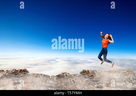 Redhead donna passa attraverso lo spazio tra le colline sulla scogliera sul cielo blu sullo sfondo. Foto Stock