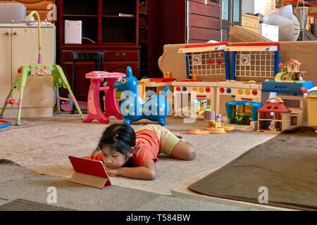Bambino con iPad. Giovane ragazza si è avvincita con il suo iPad moderno e ignorando i suoi giocattoli tradizionali. Concetto di vecchio o nuovo. Foto Stock