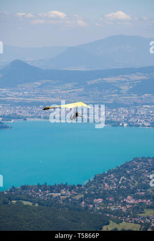Deltaplano istruttore battenti in deltaplano con il cliente al di sopra del lago di Annecy attraverso il paesaggio di montagna e città Foto Stock