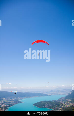 Deltaplano e parapendio volare sopra il lago di Annecy attraverso il paesaggio di montagna e città Foto Stock